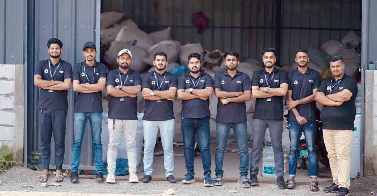 A team in matching dark shirts standing in a row with arms crossed, outside a warehouse.