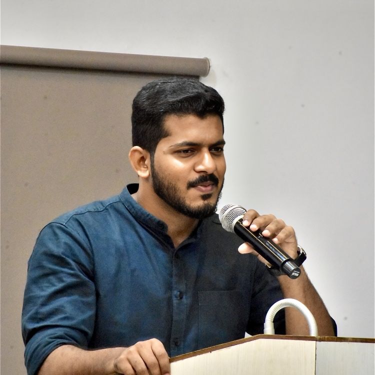 A man in a dark blue shirt speaking into a microphone at a lectern.